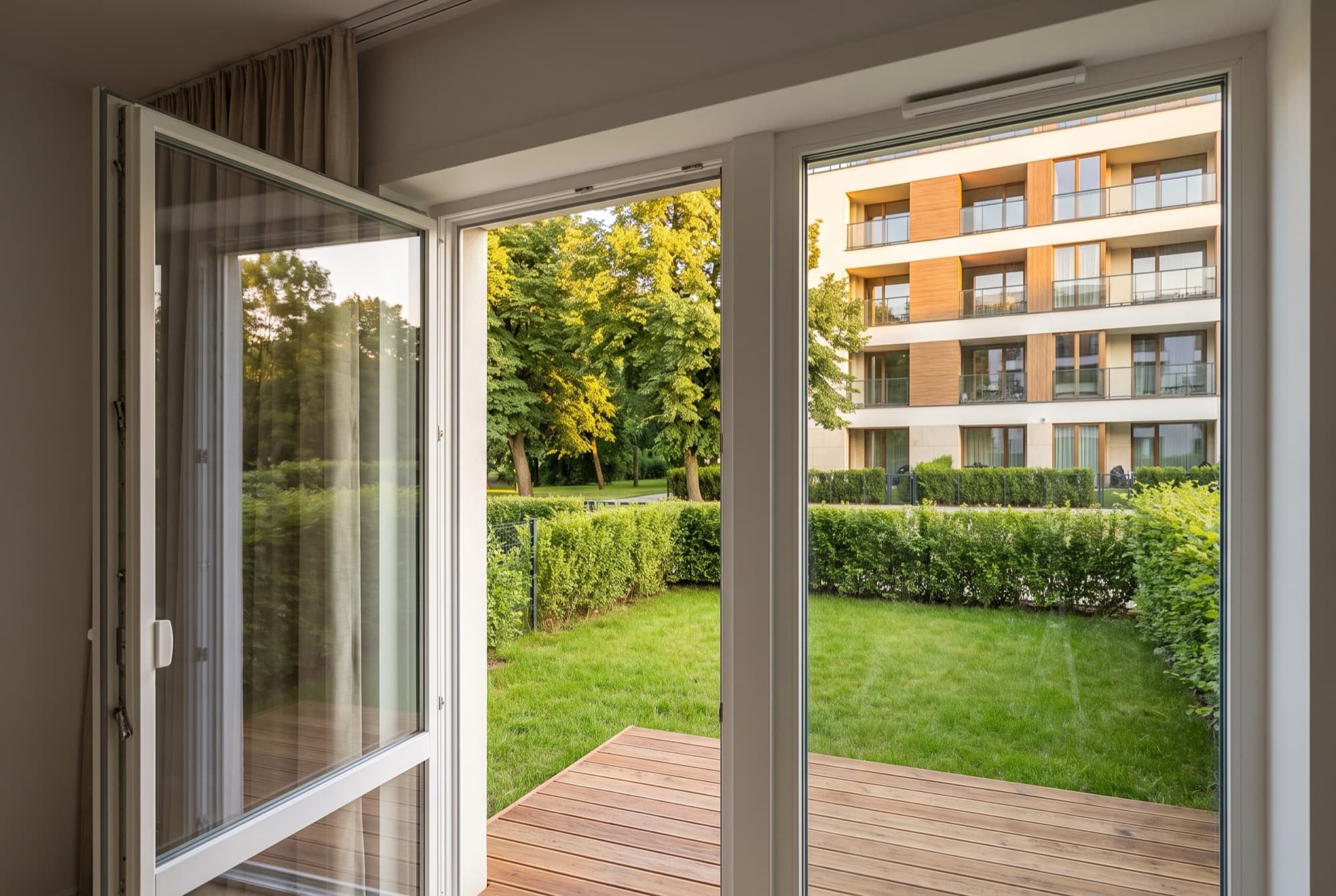 Looking out from A1's living room through open patio doors onto the decking, lawn and hedge