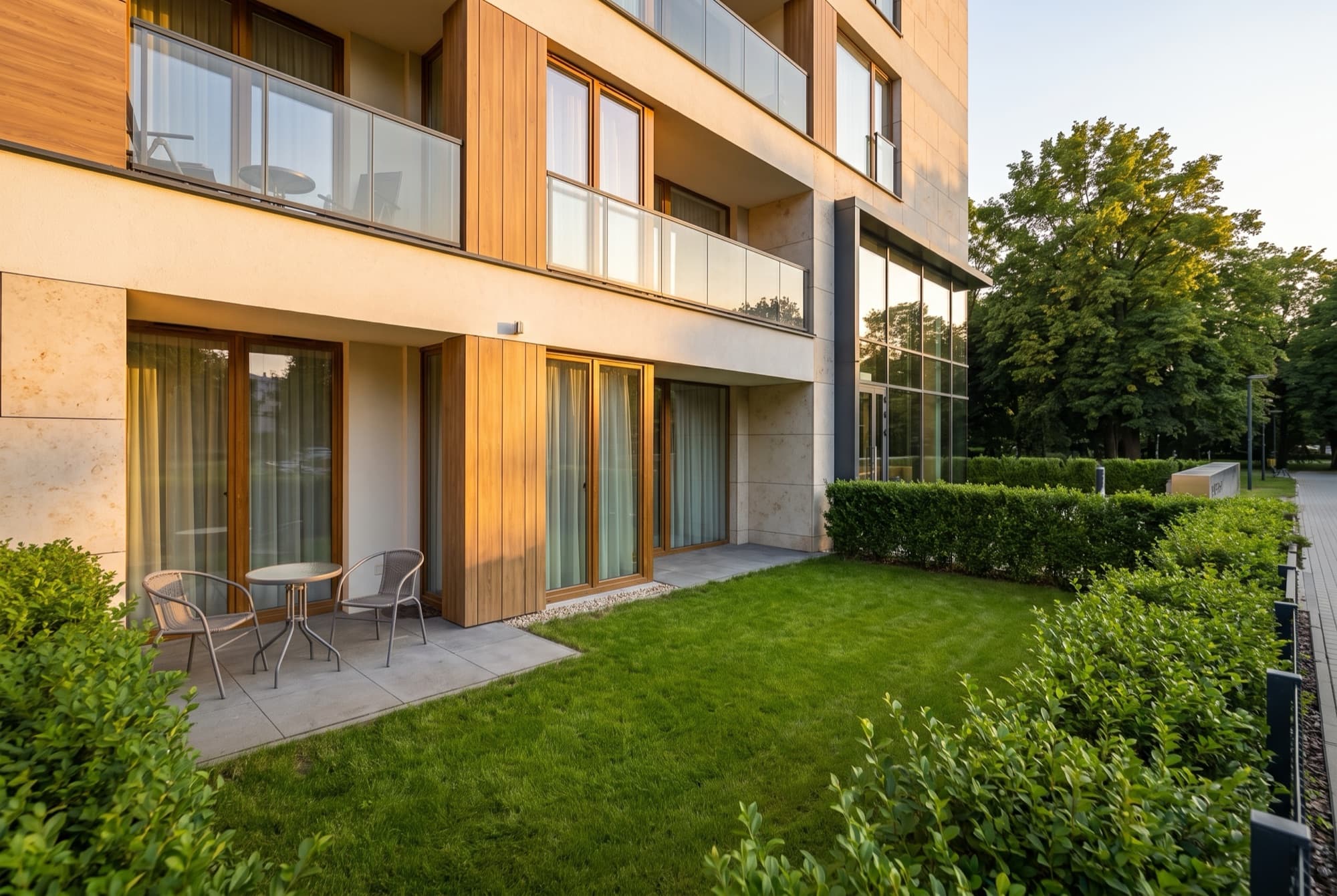 A1's fenced private garden at golden hour, lawn, clipped hedges and a bistro table on the patio below the balconies