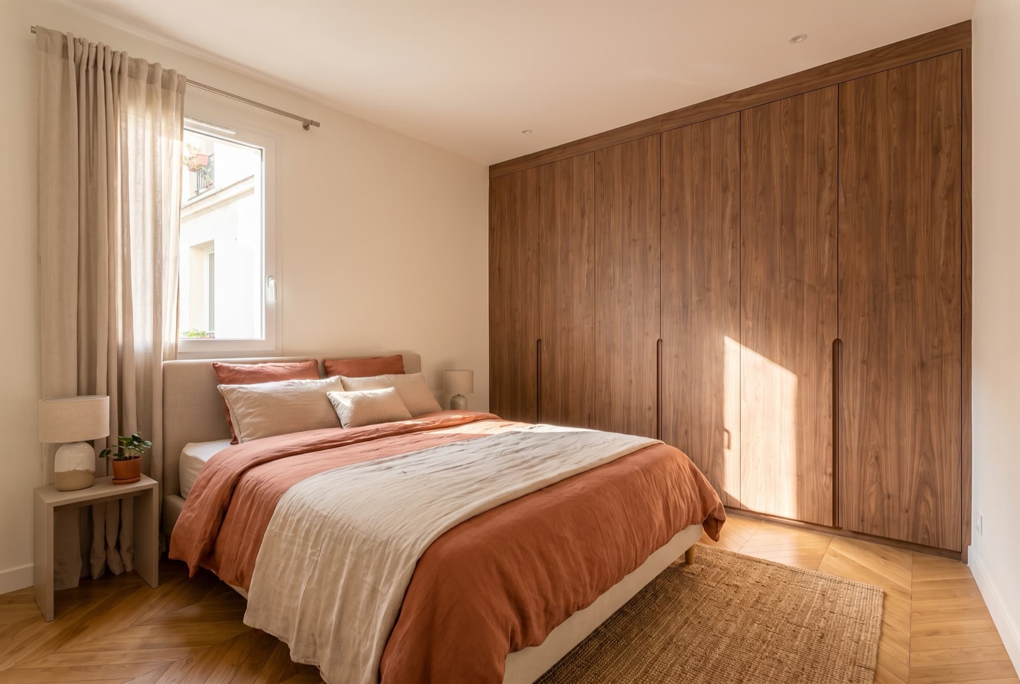 A23's master bedroom in terracotta and linen with a full wall of walnut wardrobes