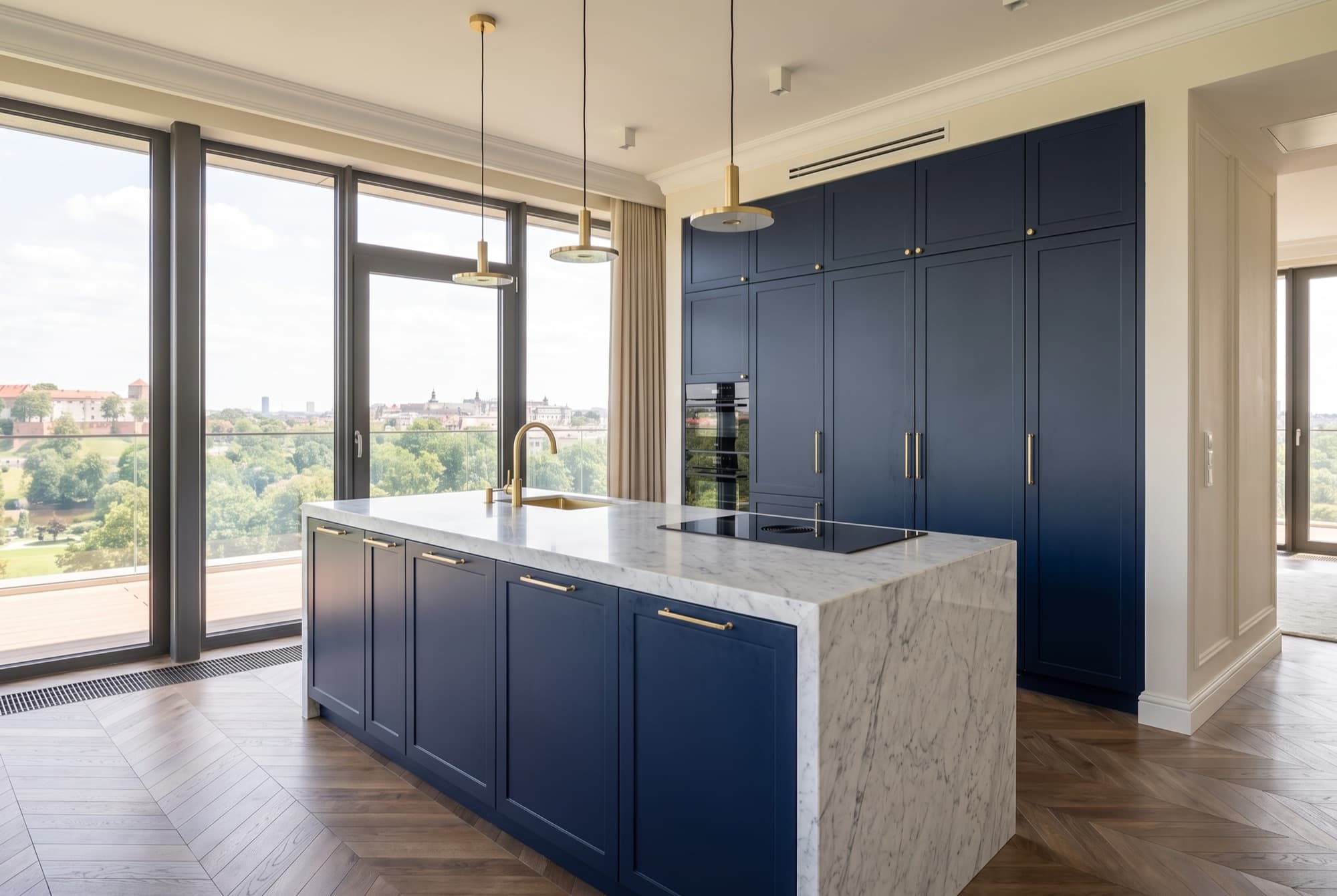 A44's navy kitchen: Carrara marble waterfall island, brass taps and pendants, glazing onto the terrace