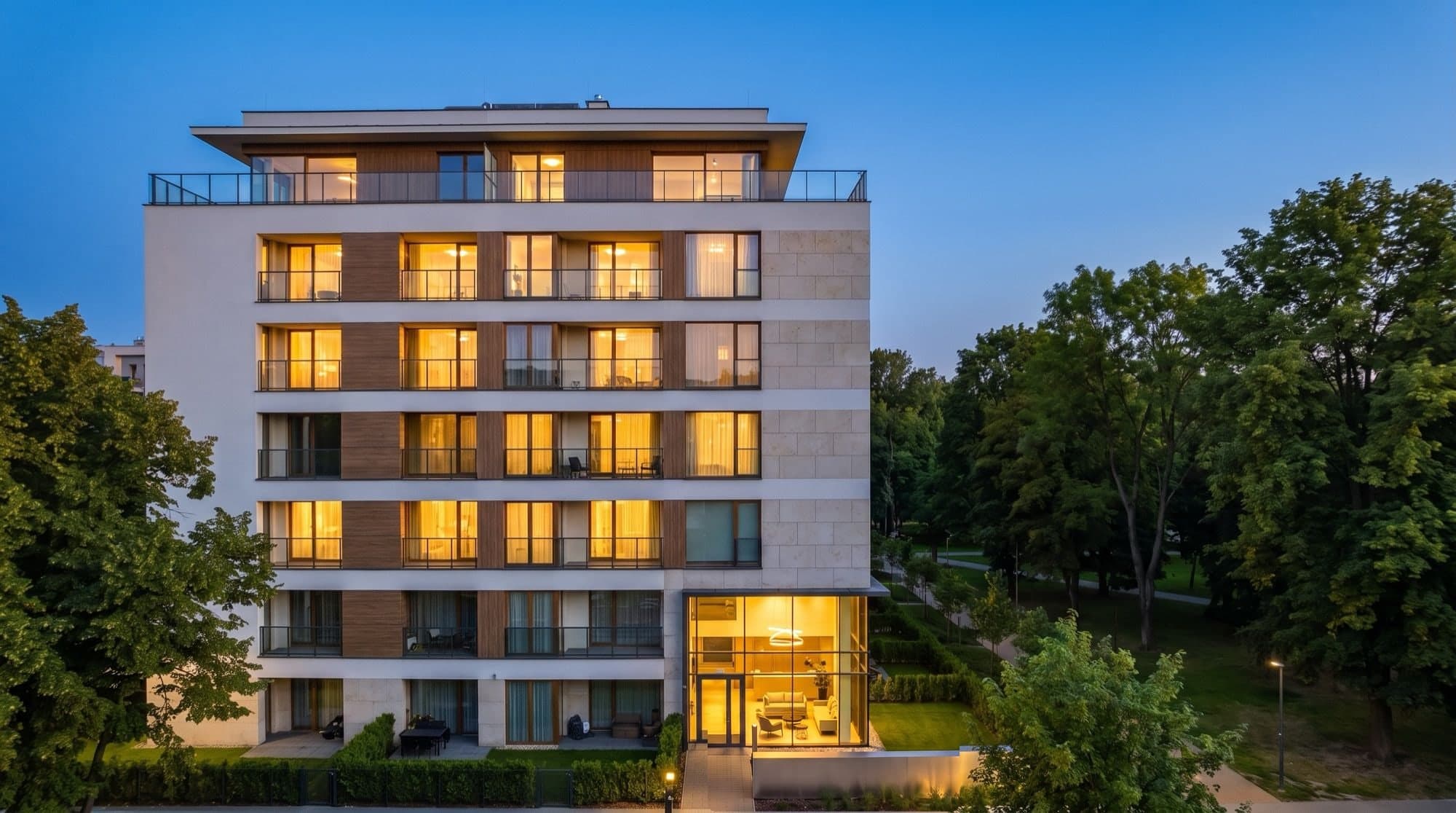Building 1 at dusk, warm-lit windows, the set-back penthouse level on top and the glazed lobby below